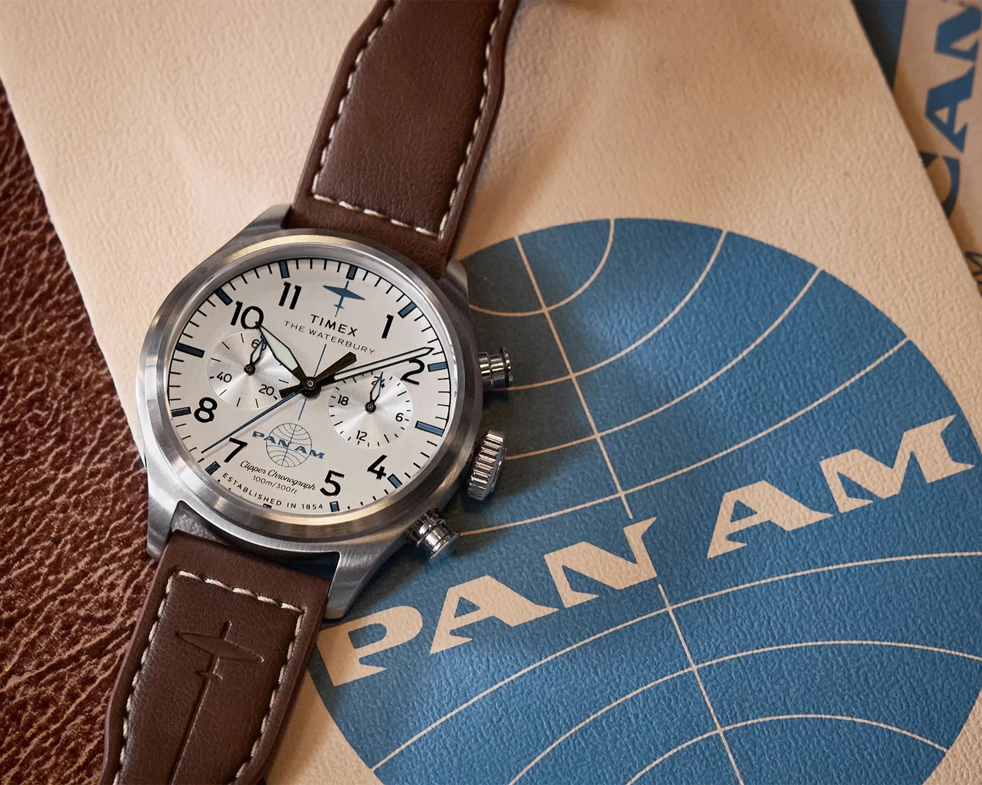 Timex Waterbury chronograph watch with white dial and brown leather strap embossed with an airplane logo on Pan Am branded paper.