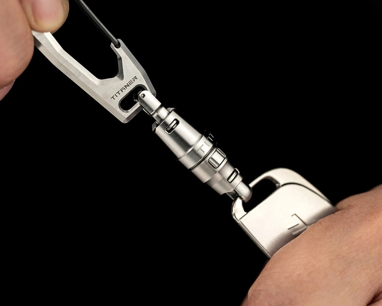 Close-up of a silver TITFNER branded metal carabiner keychain with a detachable connector held by two hands.