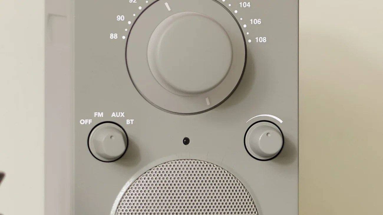 Close-up of a gray radio with three control knobs and a speaker grille.