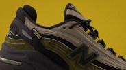 Close-up of a black and olive green New Balance sneaker with Cordura fabric tag and yellow-accented laces.