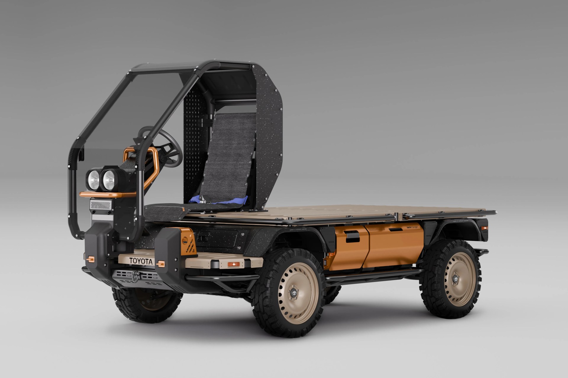 Compact flatbed utility vehicle with exposed frame, single seat, and rugged off-road tires in black and tan colors.