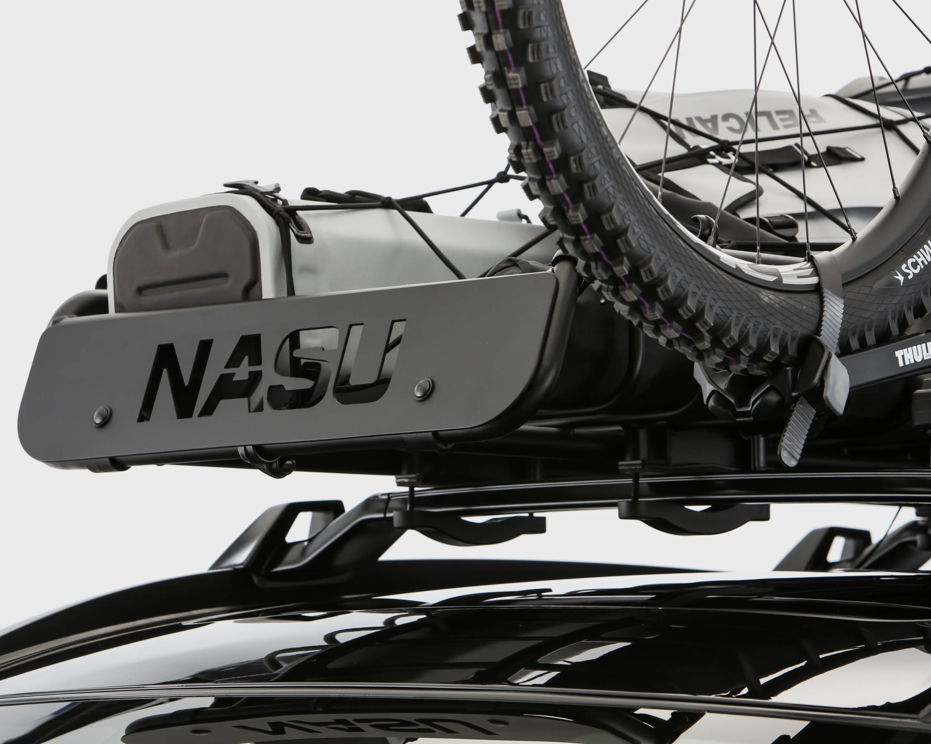 Black metal roof rack with "NASU" cutout holding a bike tire and gray storage bags on a black vehicle.