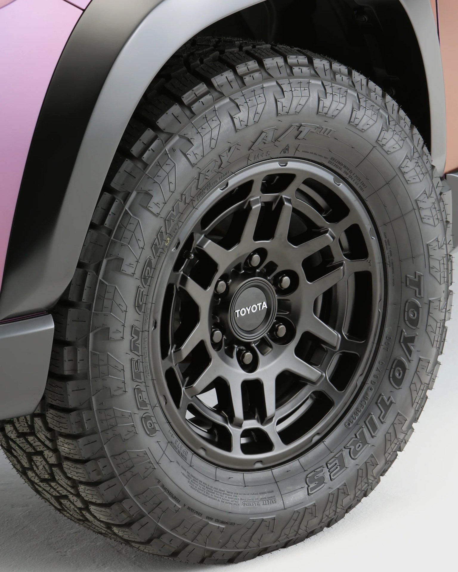 Black Toyota alloy wheel with Toyo Open Country A/T tire on a vehicle with pink and black fender.