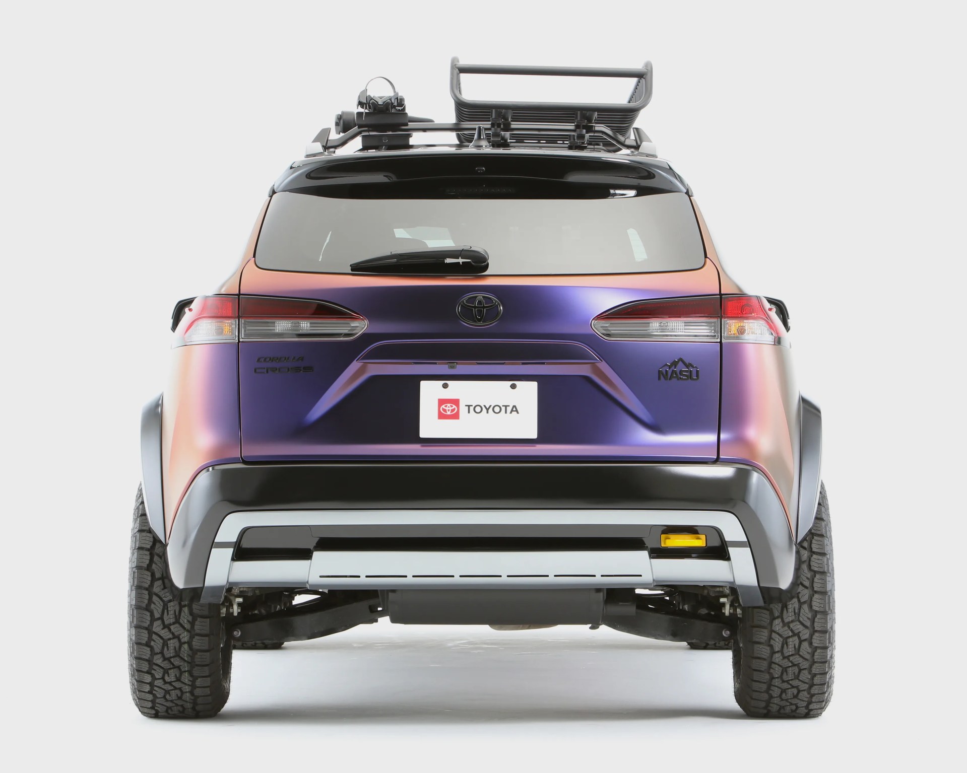 Rear view of a purple and orange Toyota Corolla Cross NASU edition with roof rack and off-road tires.