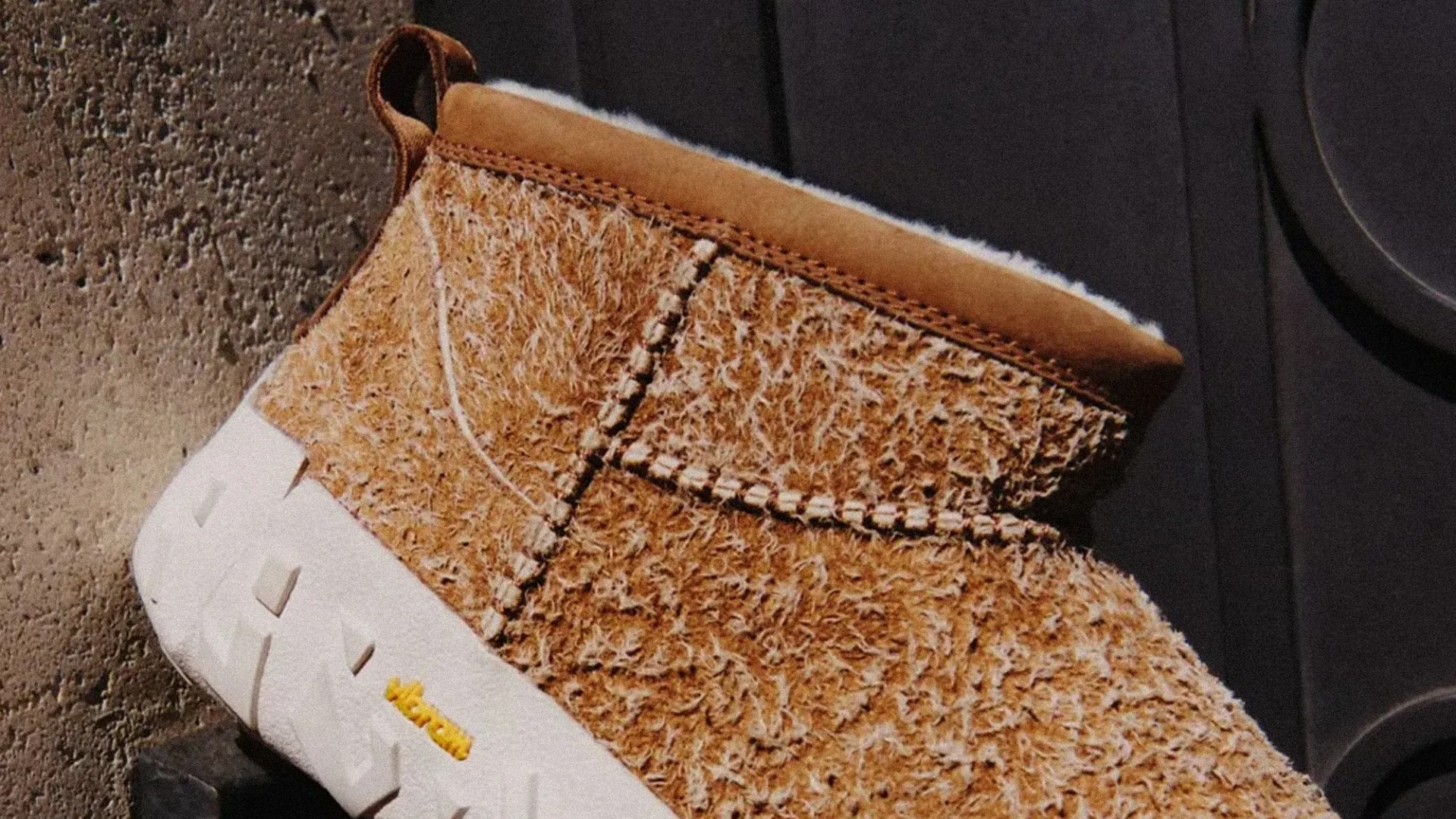 Brown fuzzy slip-on shoe with white thick sole and visible stitching on a concrete surface.