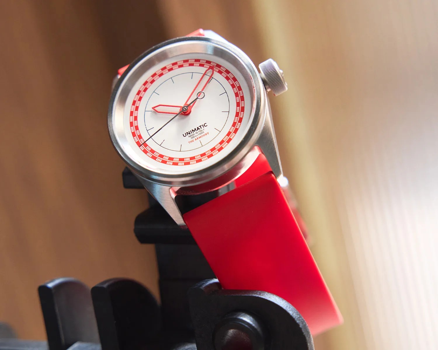 Silver wristwatch with a white dial, red markings, and a red silicone strap on a black stand.