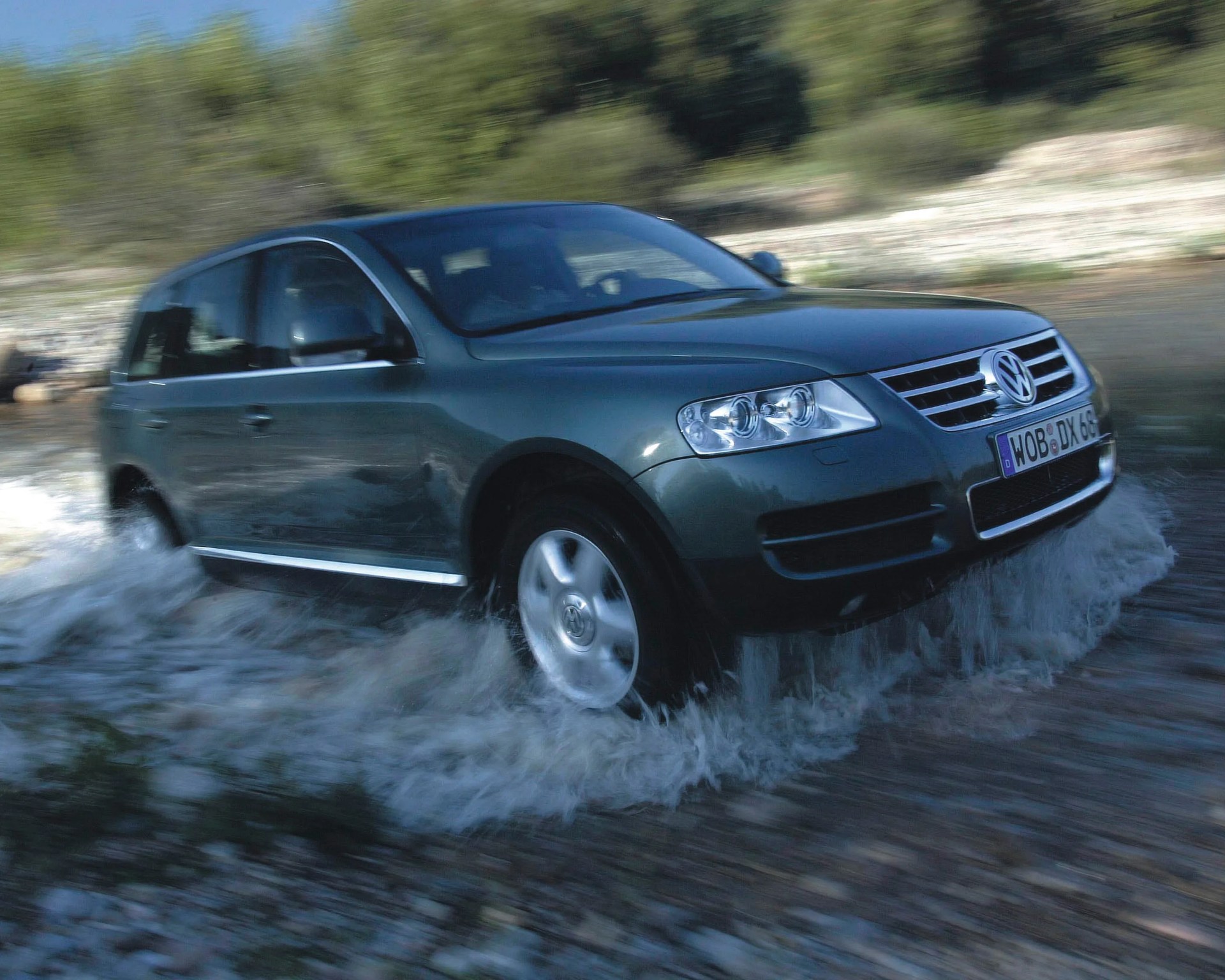 Dark green Volkswagen SUV driving through shallow water with splashing around the wheels.
