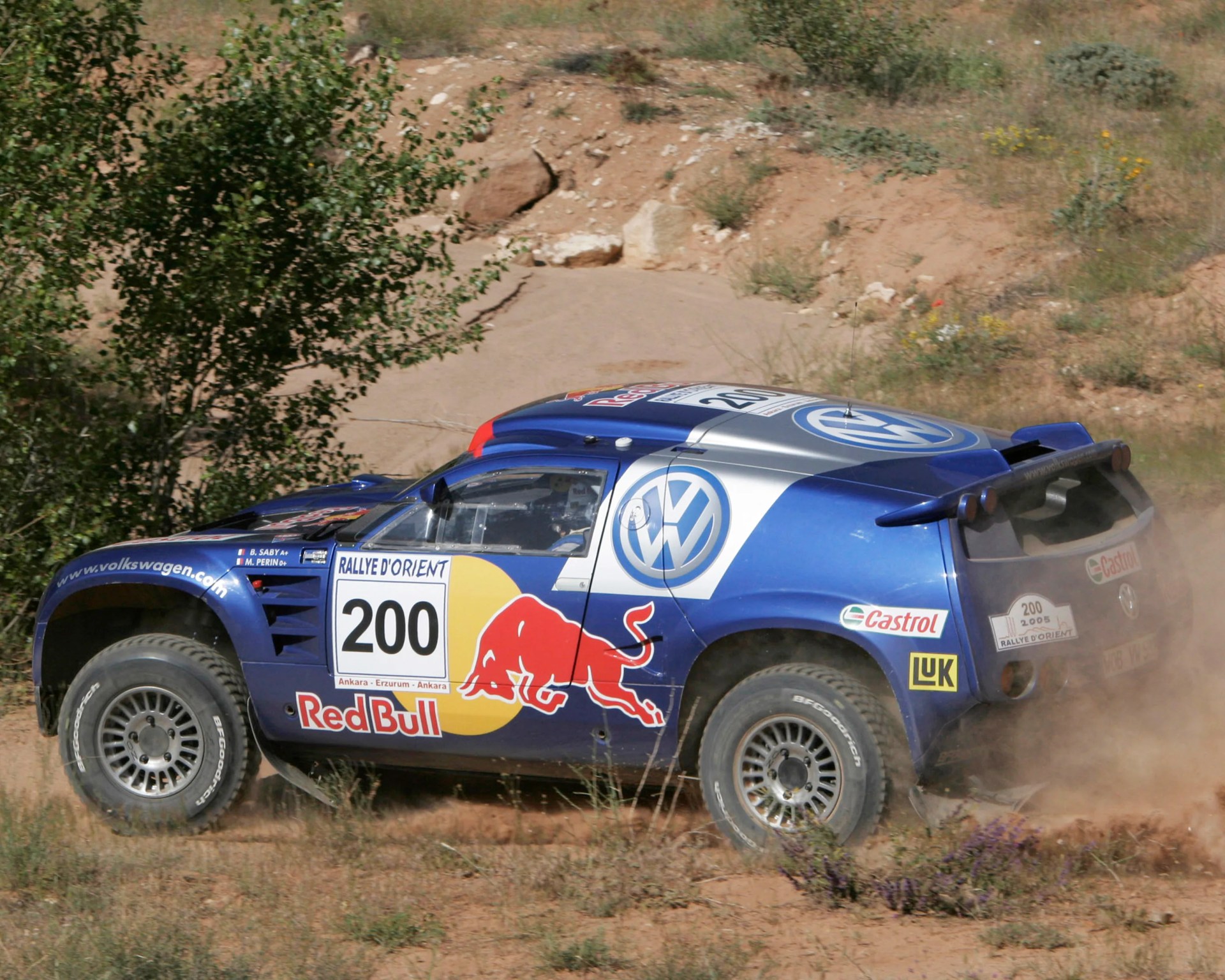 Blue Volkswagen rally car with Red Bull and Castrol logos kicking up dust on a dirt track.
