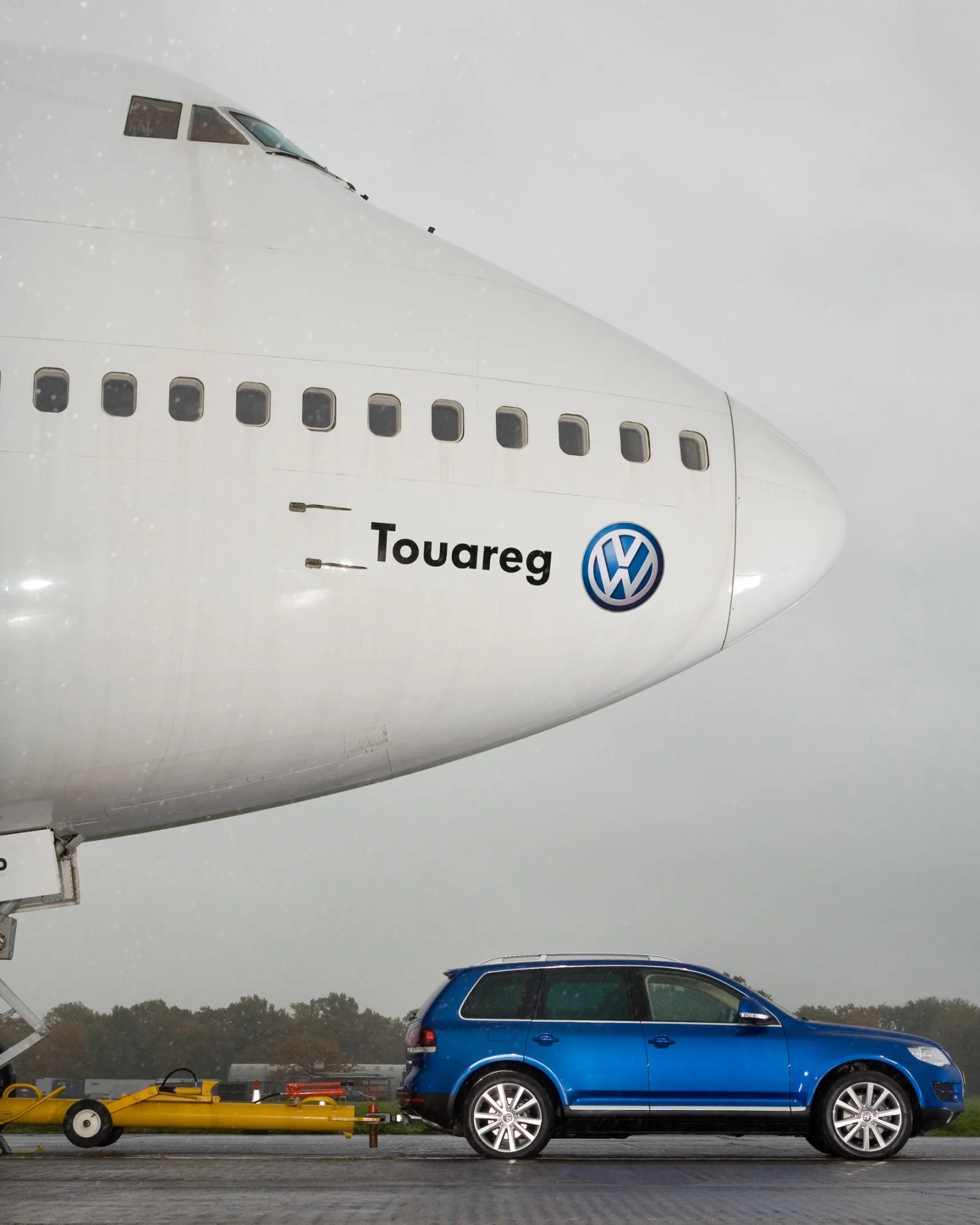 Blue Volkswagen Touareg SUV towing the nose of a large white airplane with "Touareg" and VW logo on it.