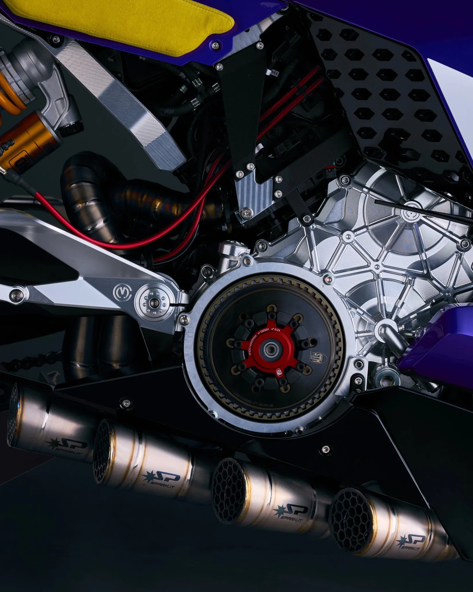 Close-up of a motorcycle engine and exhaust system with silver, black, and red components and yellow seat detail.