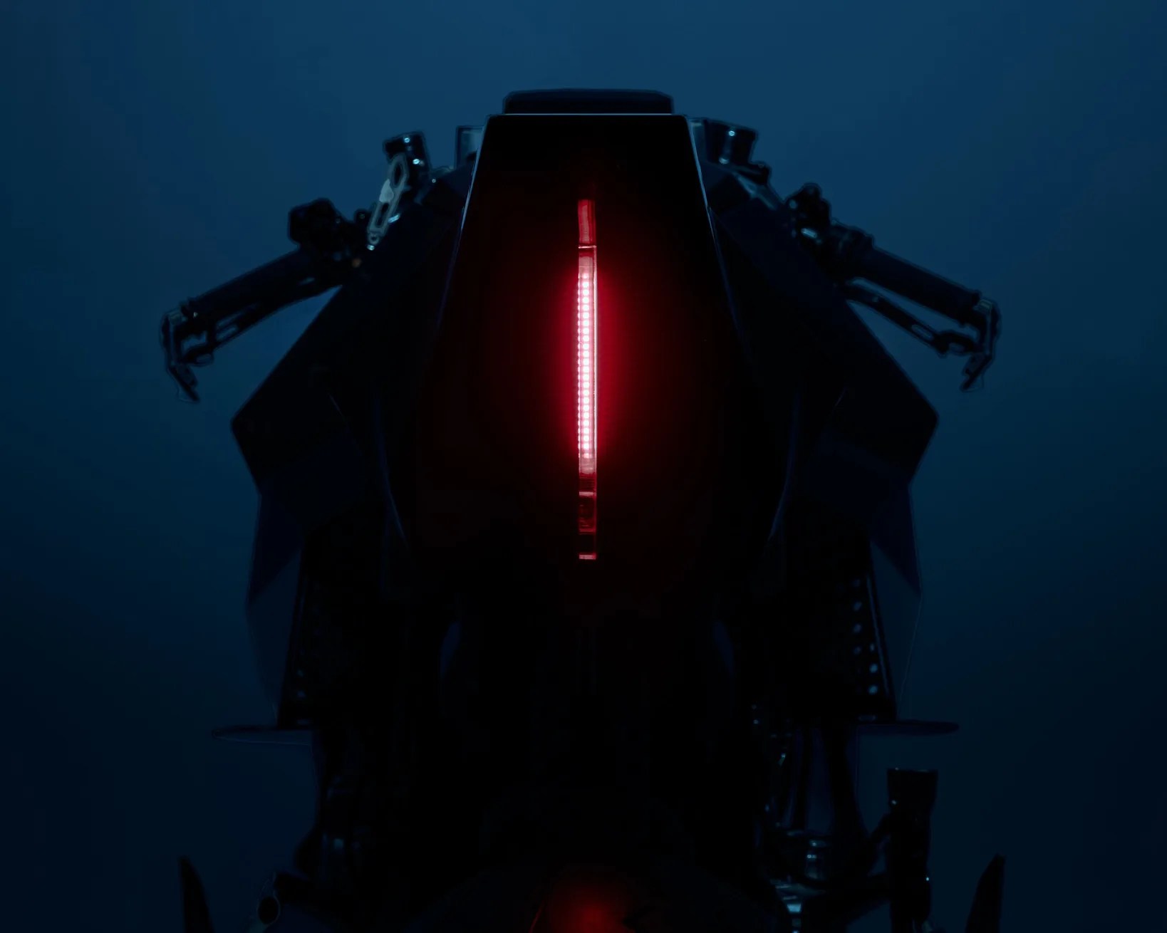 Rear view of a motorcycle with a vertical red LED tail light glowing in a dark setting.