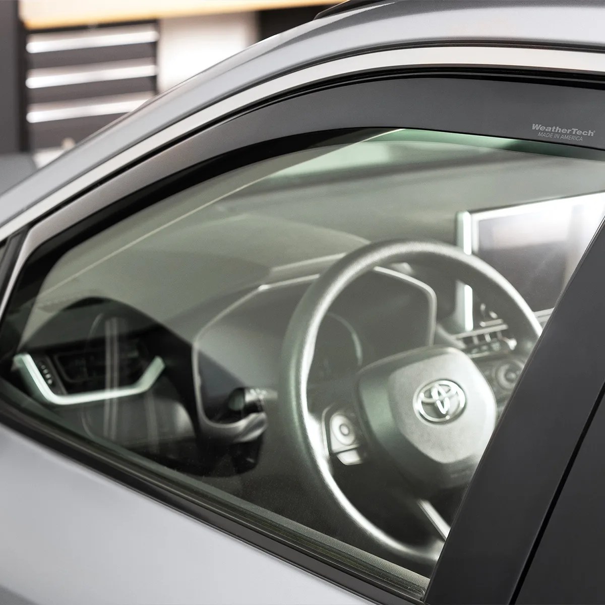 Car window visor with WeatherTech logo installed on a silver vehicle's front side window.