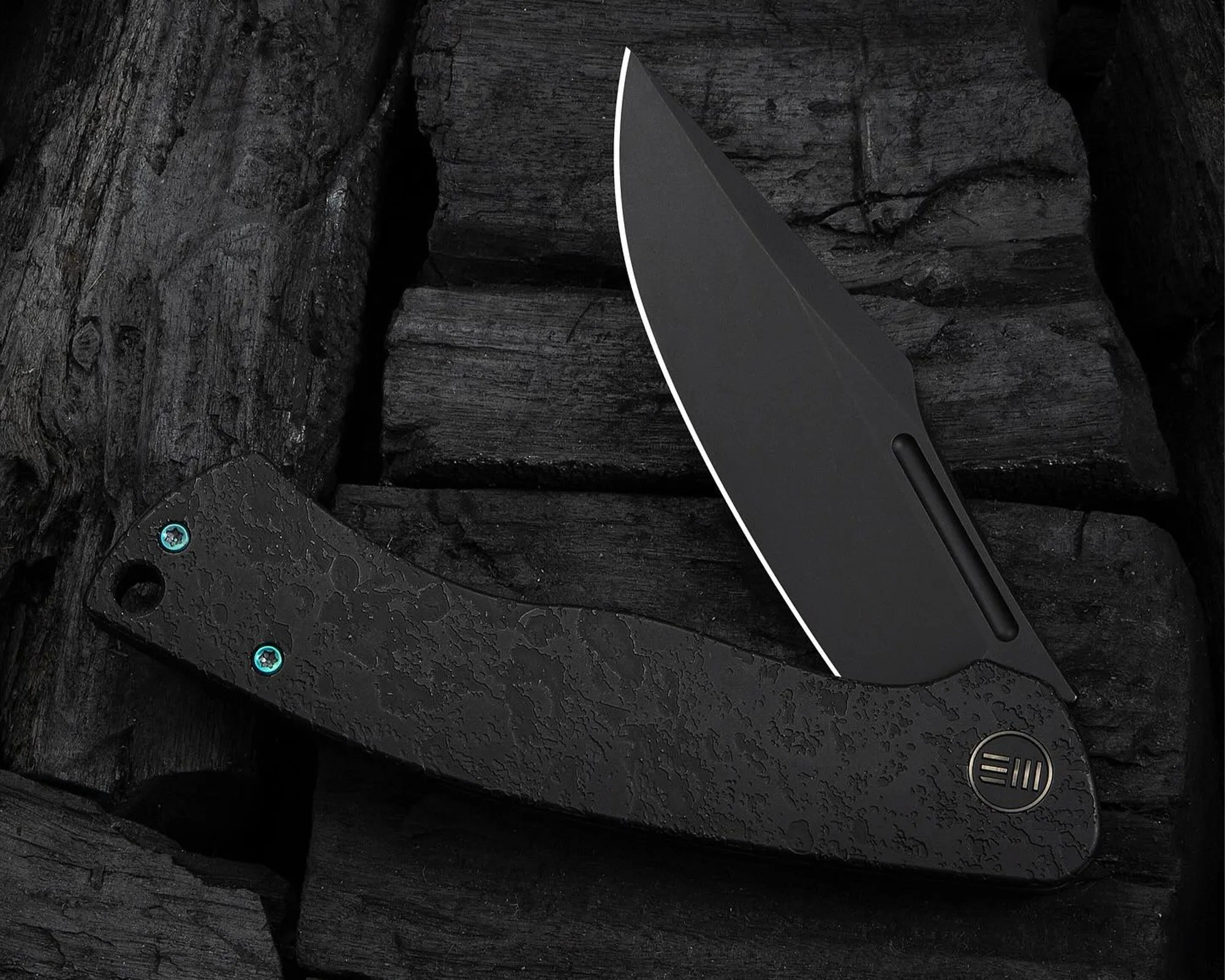 Black folding knife with textured handle and partially open matte black blade on dark wooden surface.