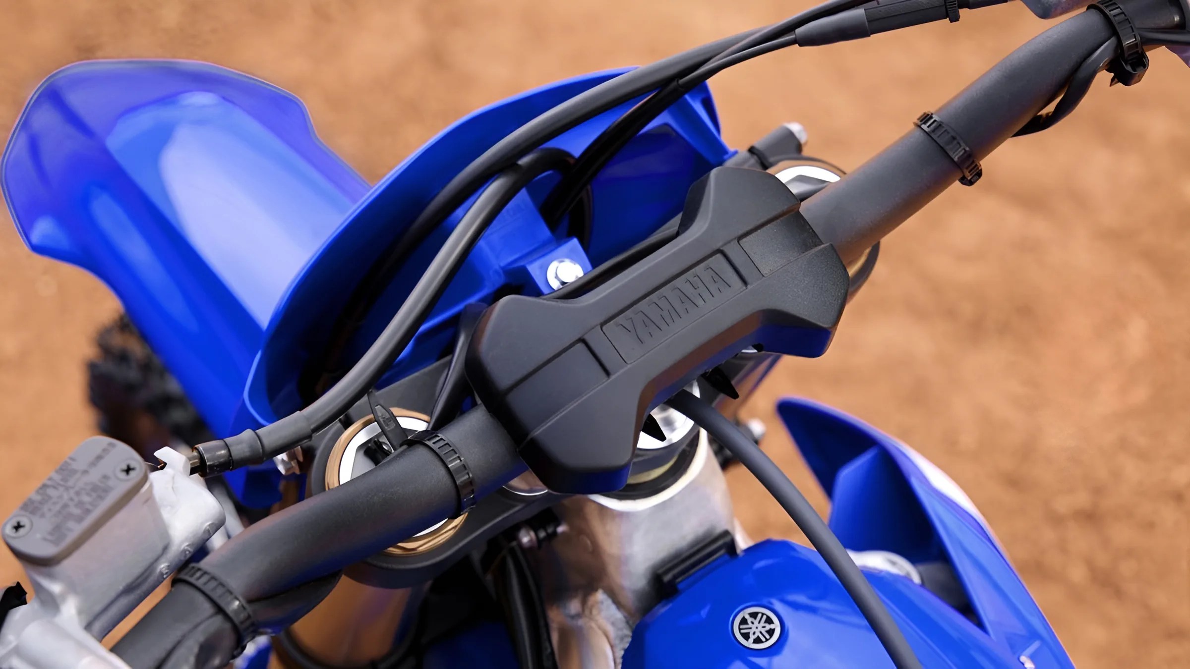 Close-up of blue Yamaha dirt bike handlebars with black grips and protective pad on a dirt surface.