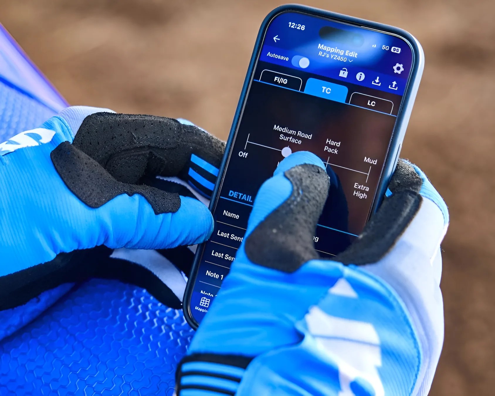 Person wearing blue and black gloves adjusting a slider on a smartphone screen showing terrain mapping options.