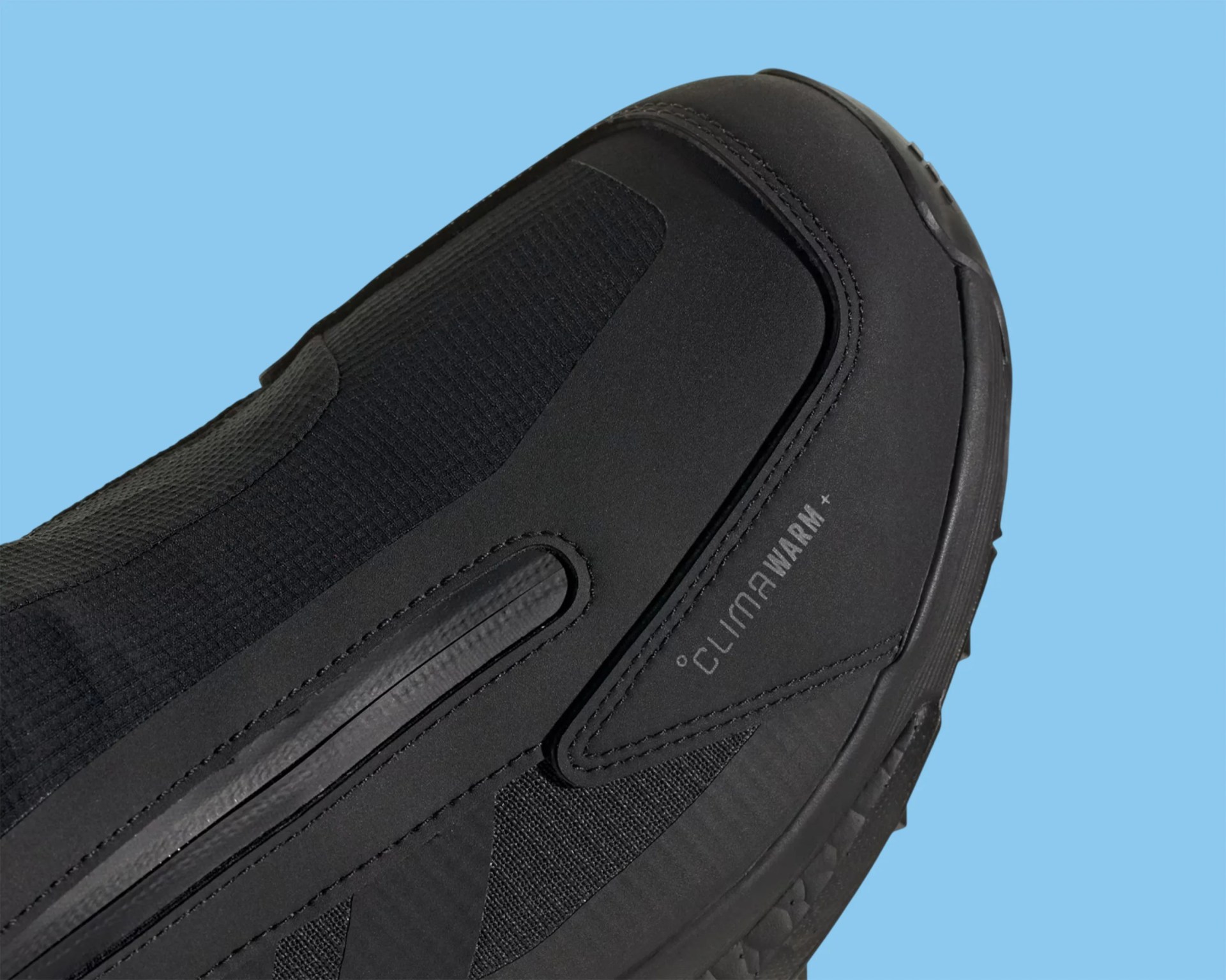 Close-up of the black shoe toe area with "CLIMAWARM+" text on the side against a blue background.