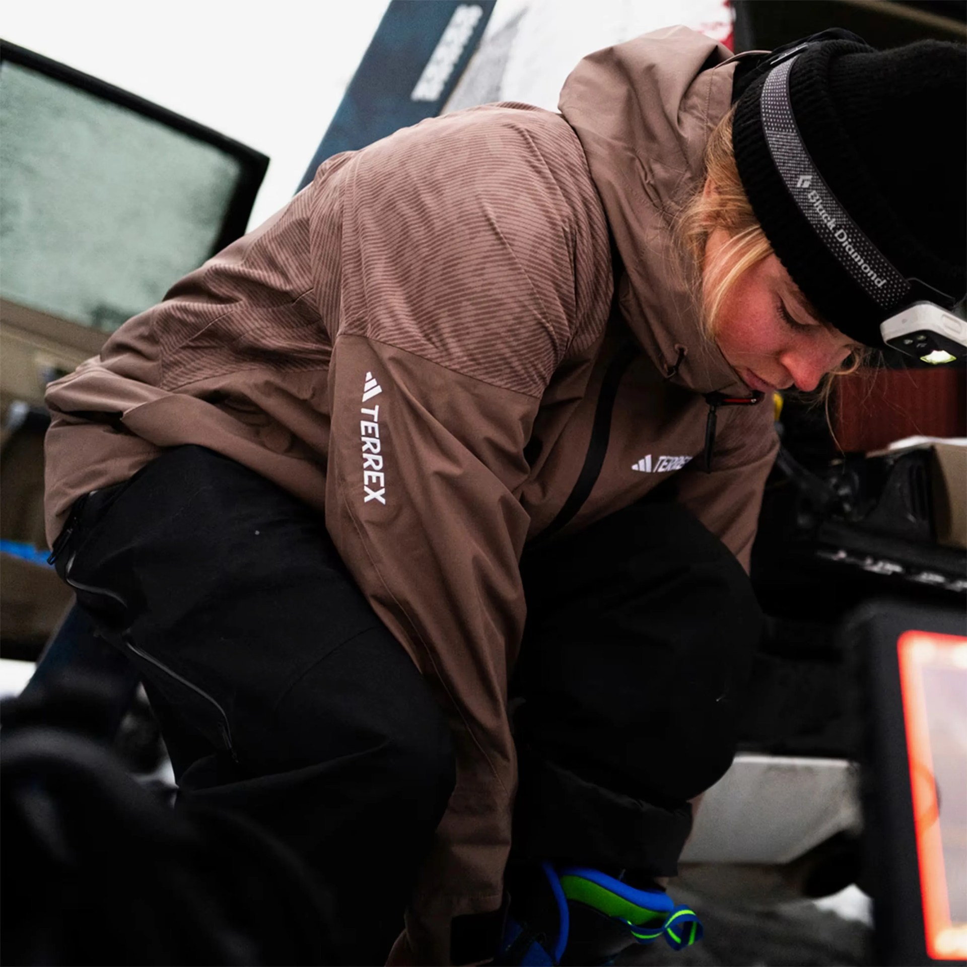 Person wearing a brown Terrex jacket and black pants, crouching near a vehicle door.