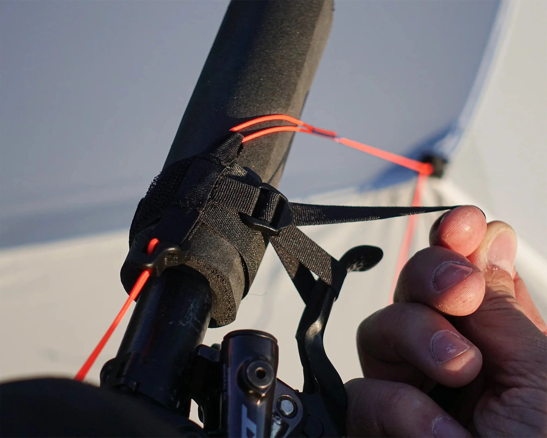 Close-up of a hand adjusting a black strap with red cord attached to a bicycle handlebar.