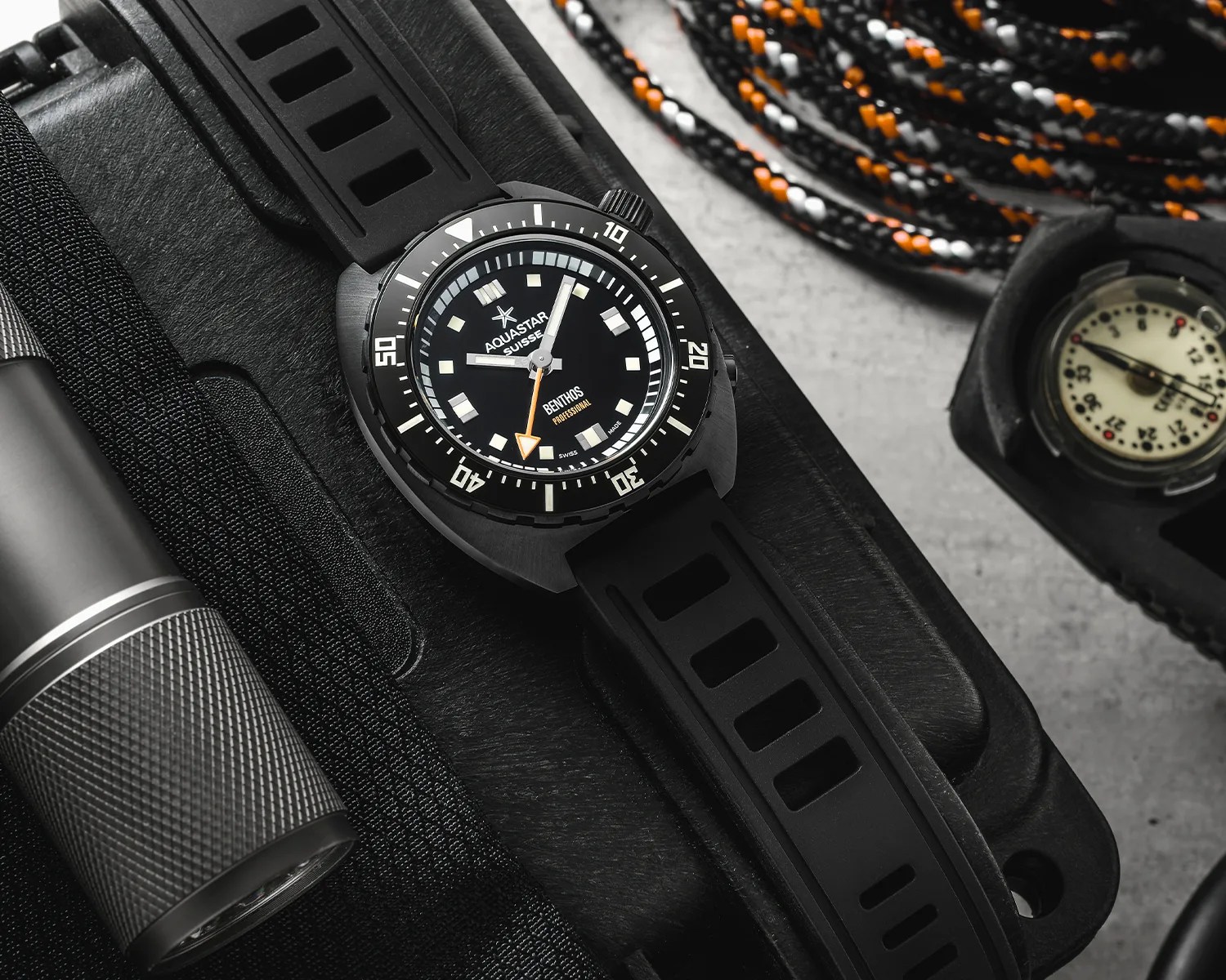 Black Aquastar Benthos Professional dive watch with black rubber strap on a black case next to a flashlight and a compass.