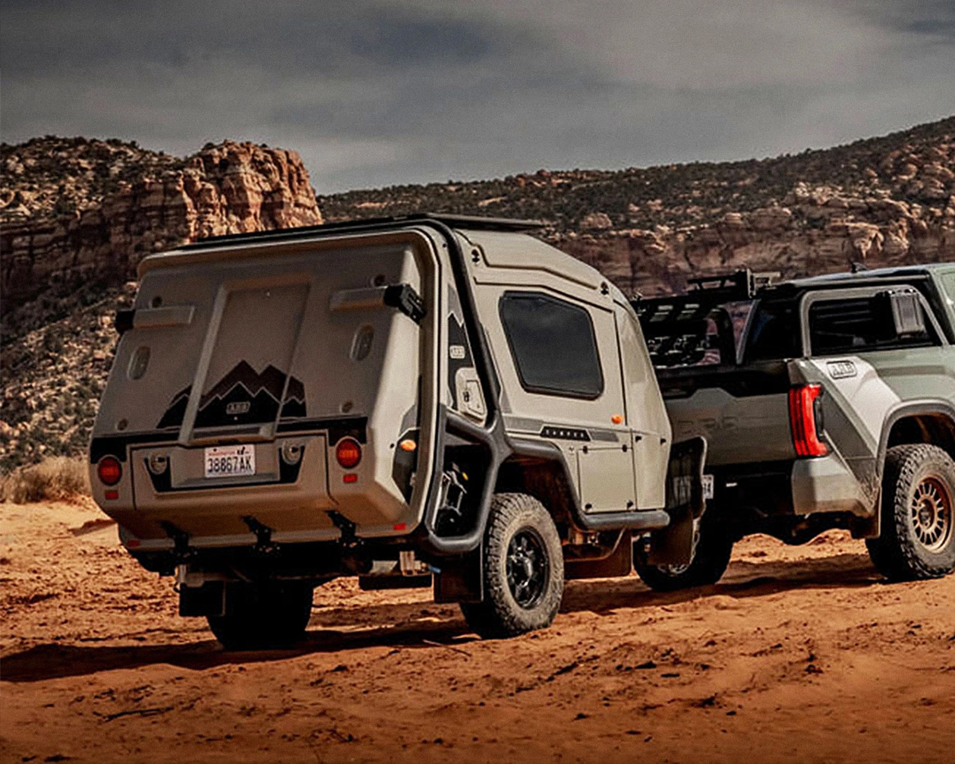 Compact beige off-road camper trailer hitched to a rugged pickup truck on a desert trail.