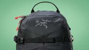 Black Arc'teryx backpack with red zipper pulls and a top handle against a green background.
