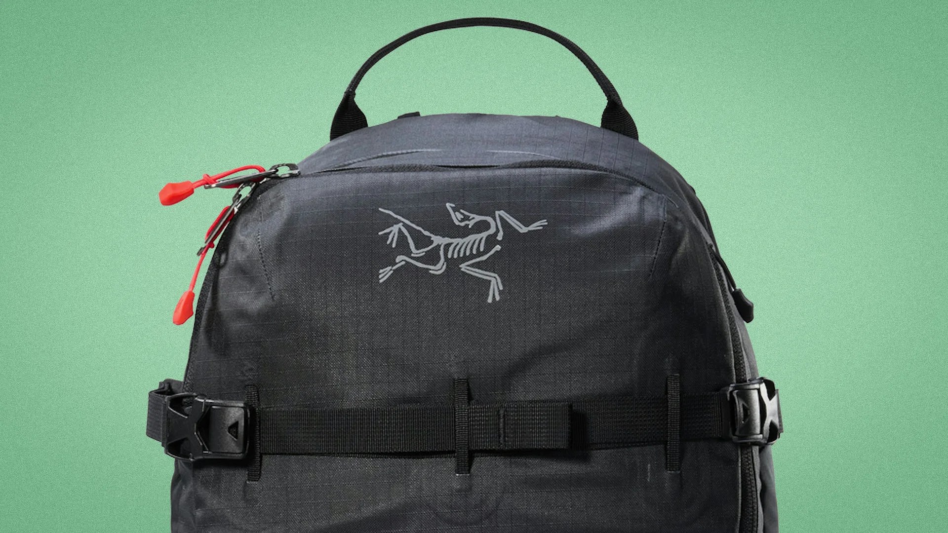 Black Arc'teryx backpack with red zipper pulls and a top handle against a green background.