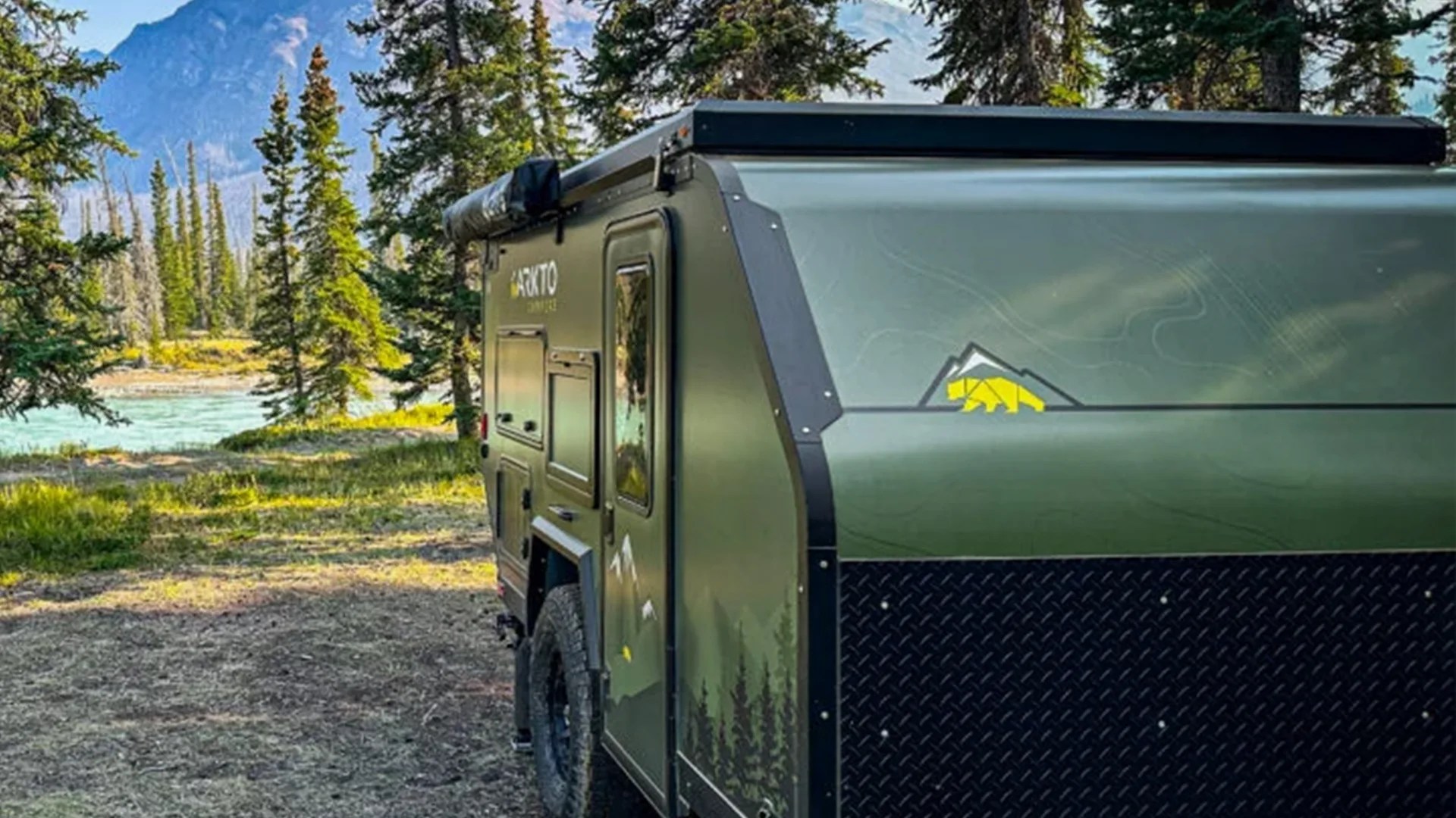 Green off-road camper trailer with black diamond plate panel and mountain bear logo parked in forested area.