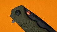 Close-up of a folding knife with a textured dark green handle and a black blade against an orange background.