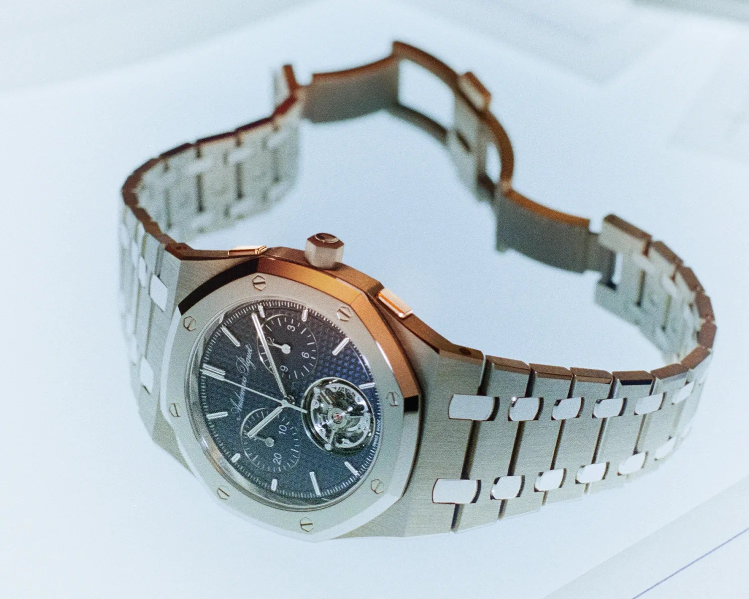 Silver metal wristwatch with a blue textured dial and visible tourbillon mechanism on a white surface.