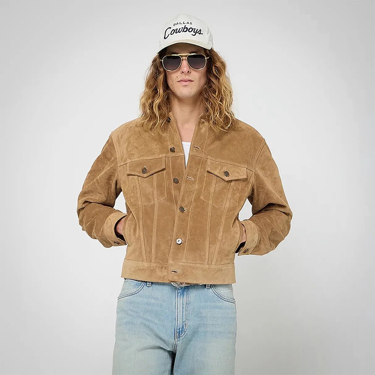 Tan suede button-up jacket with chest pockets worn by a person in light blue jeans and a white cap.