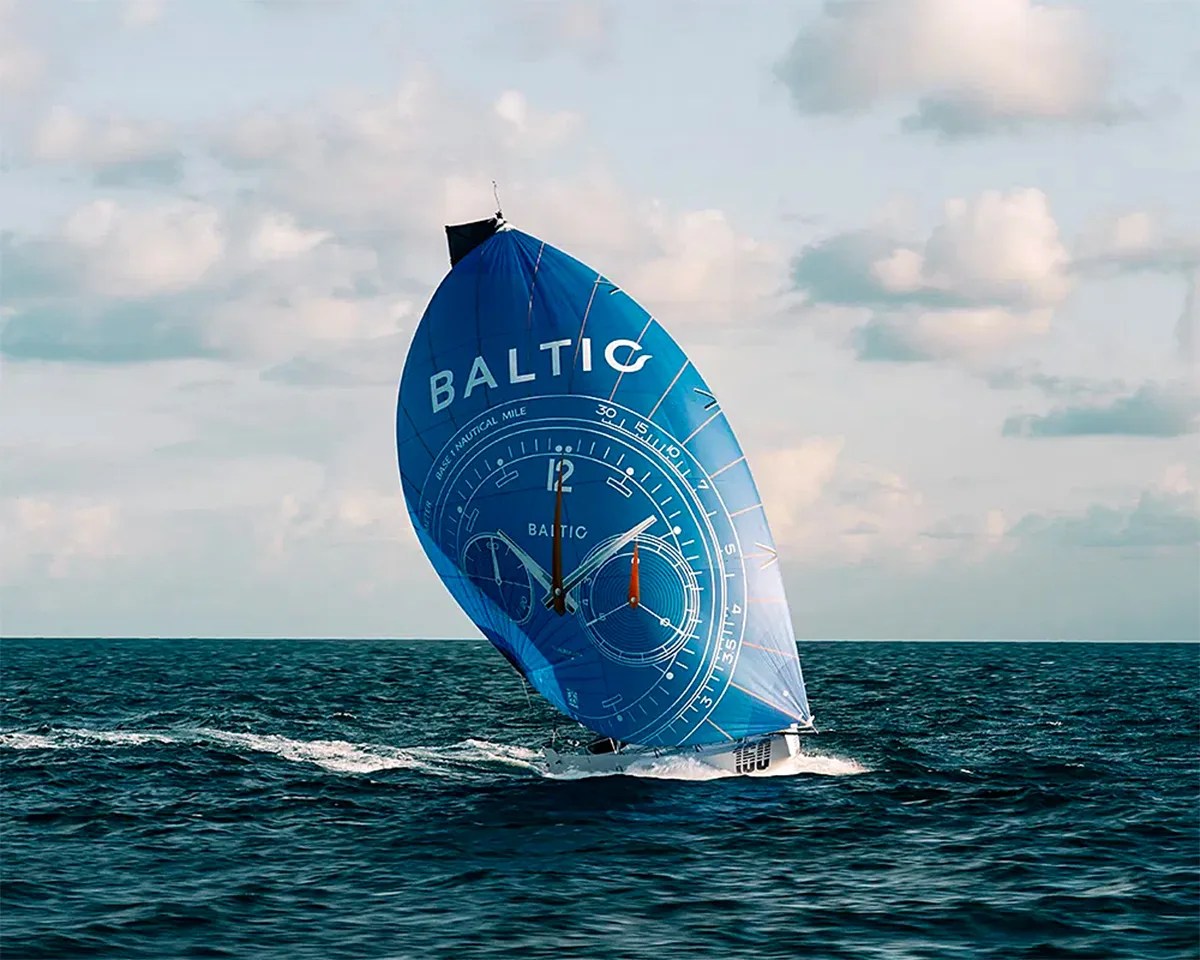 Sailboat on the ocean with a large blue sail featuring a watch face design and the word "BALTIC.
