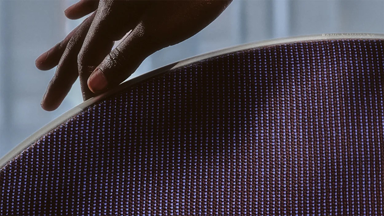 Hand touching the edge of a round speaker grille with a textured purple fabric surface.