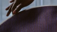 Hand touching the edge of a round speaker grille with a textured purple fabric surface.