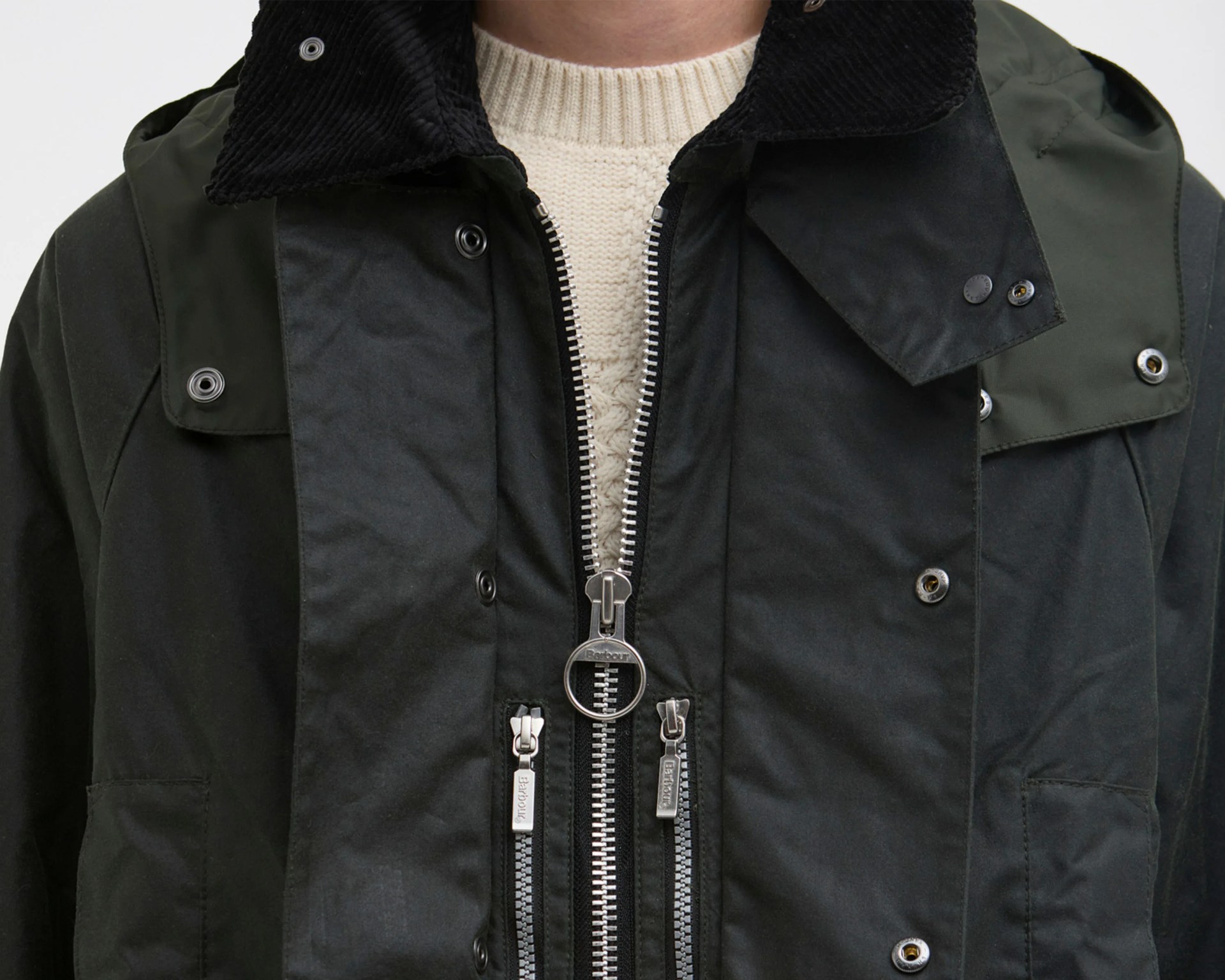 Close-up of a black jacket with silver zippers and snap buttons over a cream knit sweater.