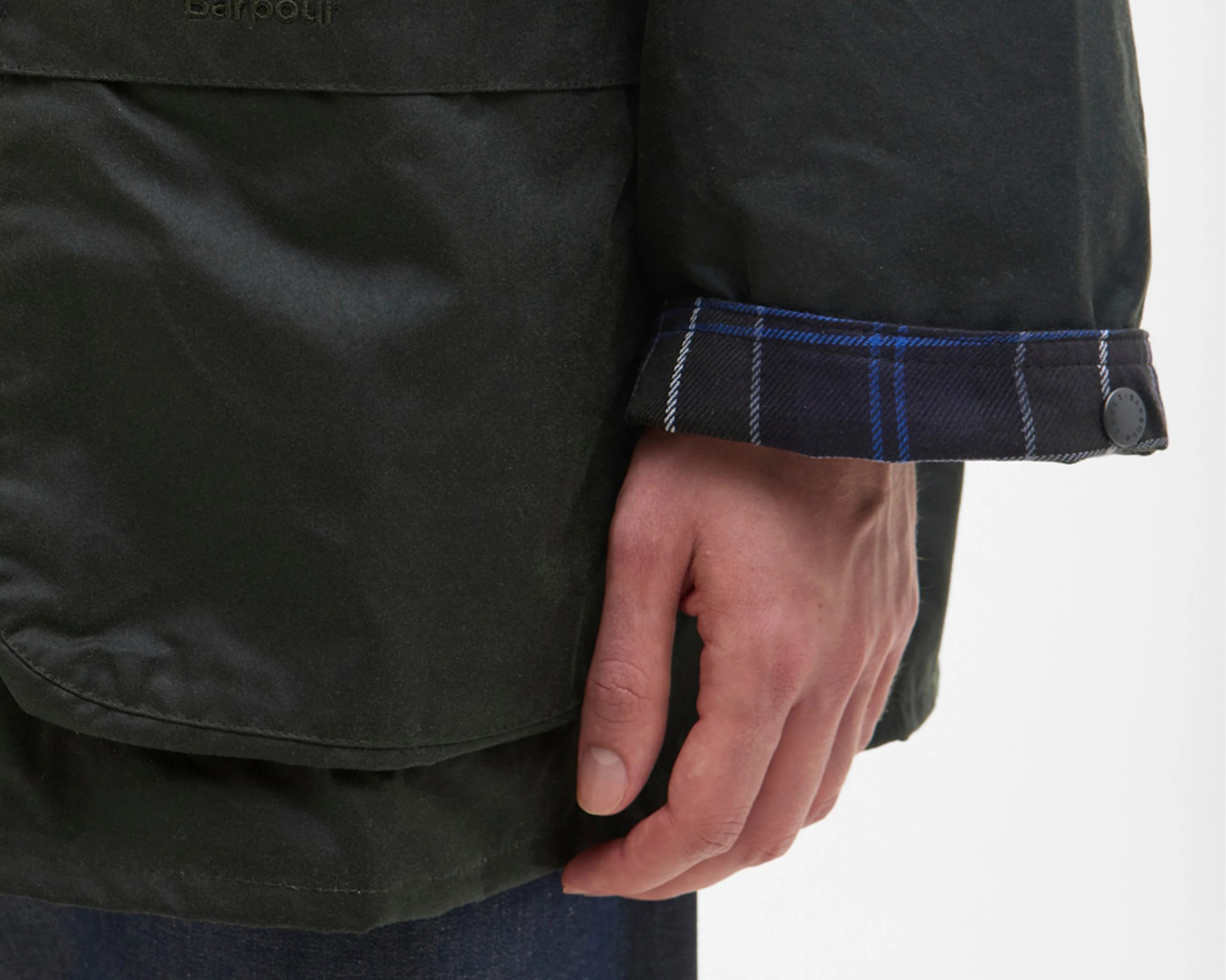 Close-up of a black jacket sleeve with blue plaid cuff and a hand resting beside it.