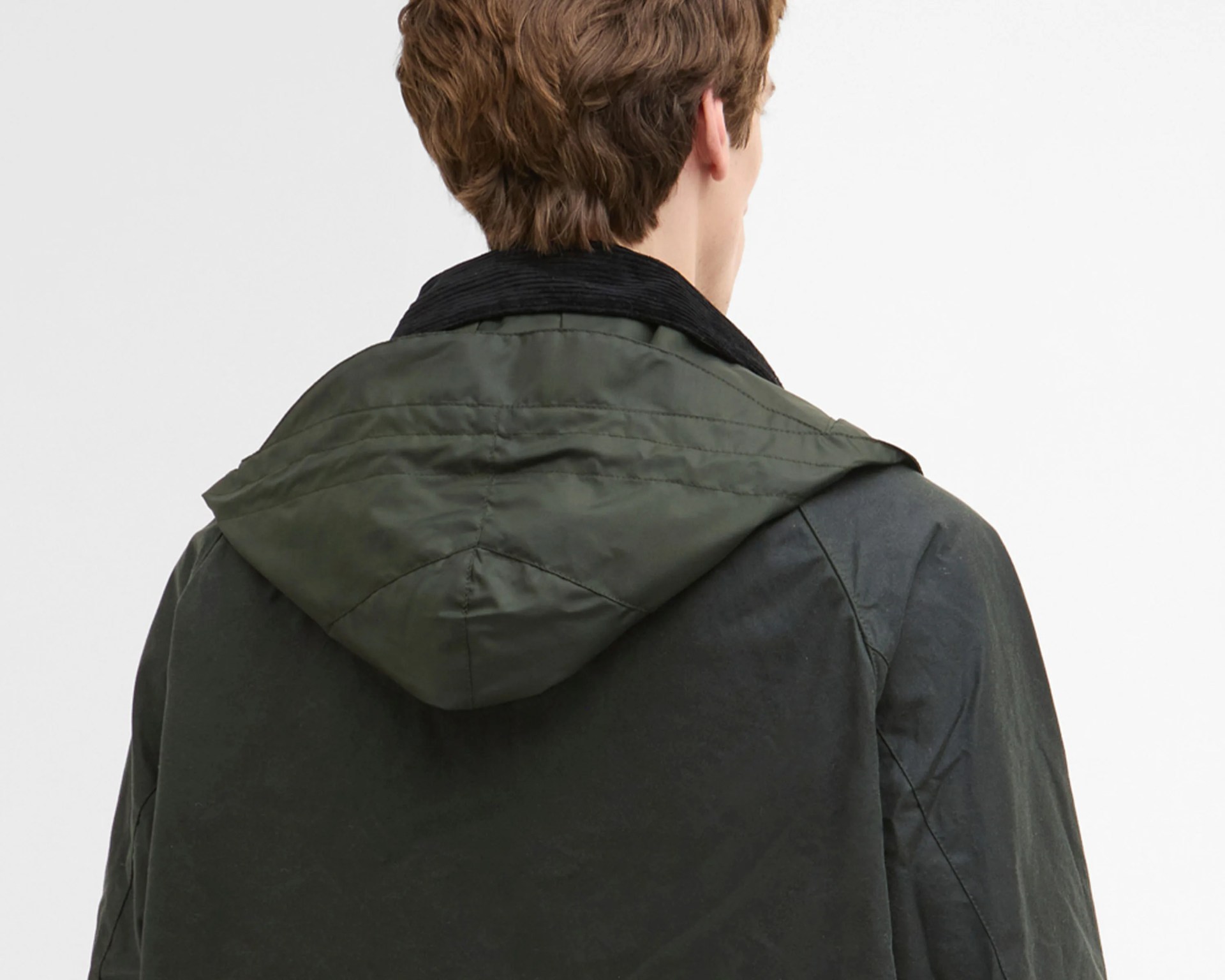 Back view of a person wearing a dark green jacket with a hood and a black corduroy collar.