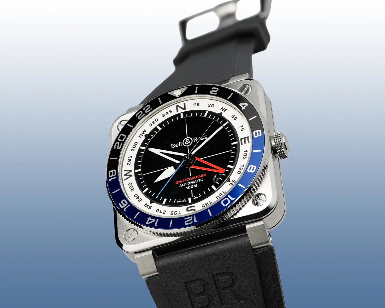 Square stainless steel Bell & Ross wristwatch with black dial, blue and black bezel, and black rubber strap.