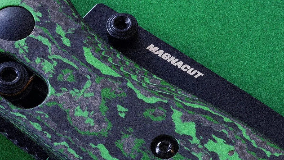 Close-up of a green and black patterned knife handle with the word "MAGNACUT" on the black blade.