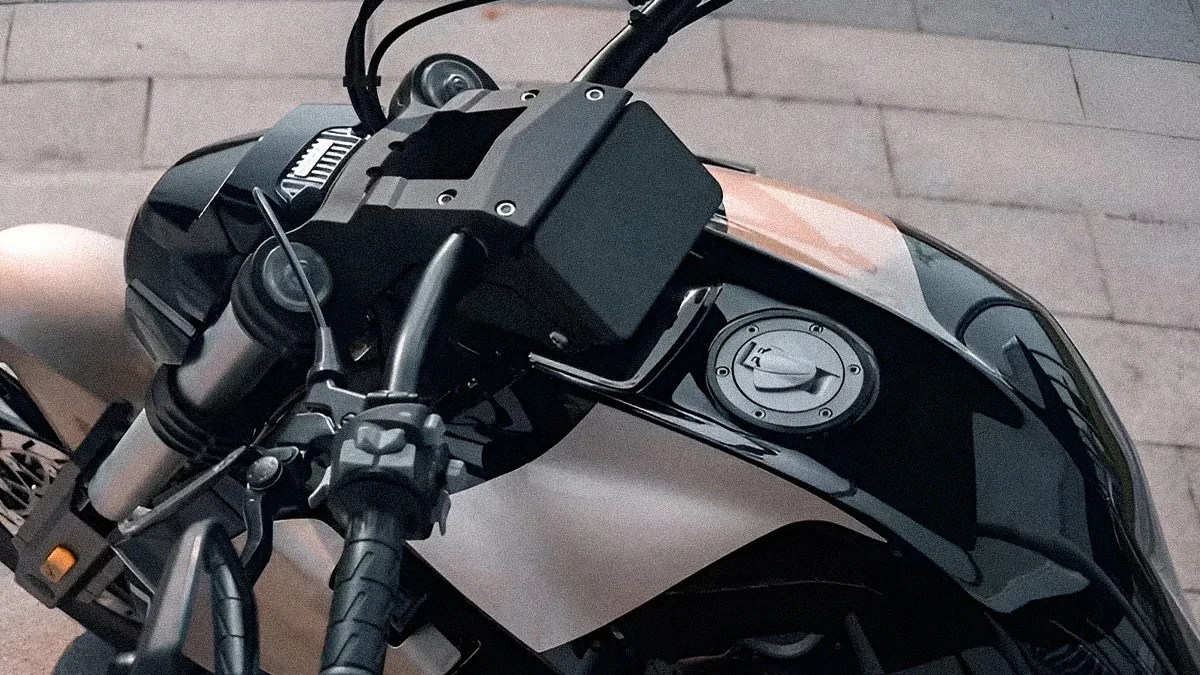 Close-up of a black motorcycle fuel tank and handlebar controls on a paved surface.