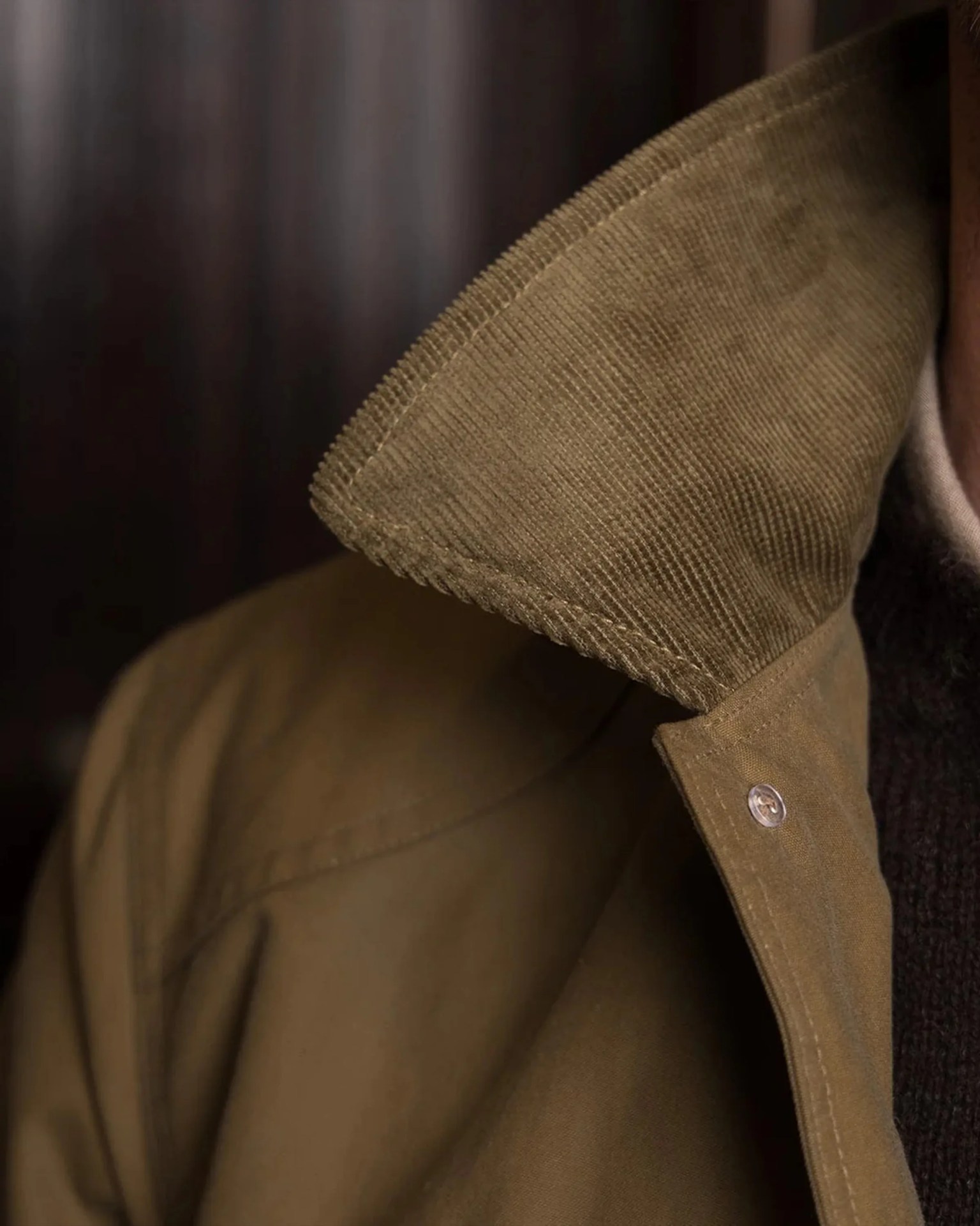 Close-up of a brown corduroy collar on a khaki jacket worn over a dark knit sweater.