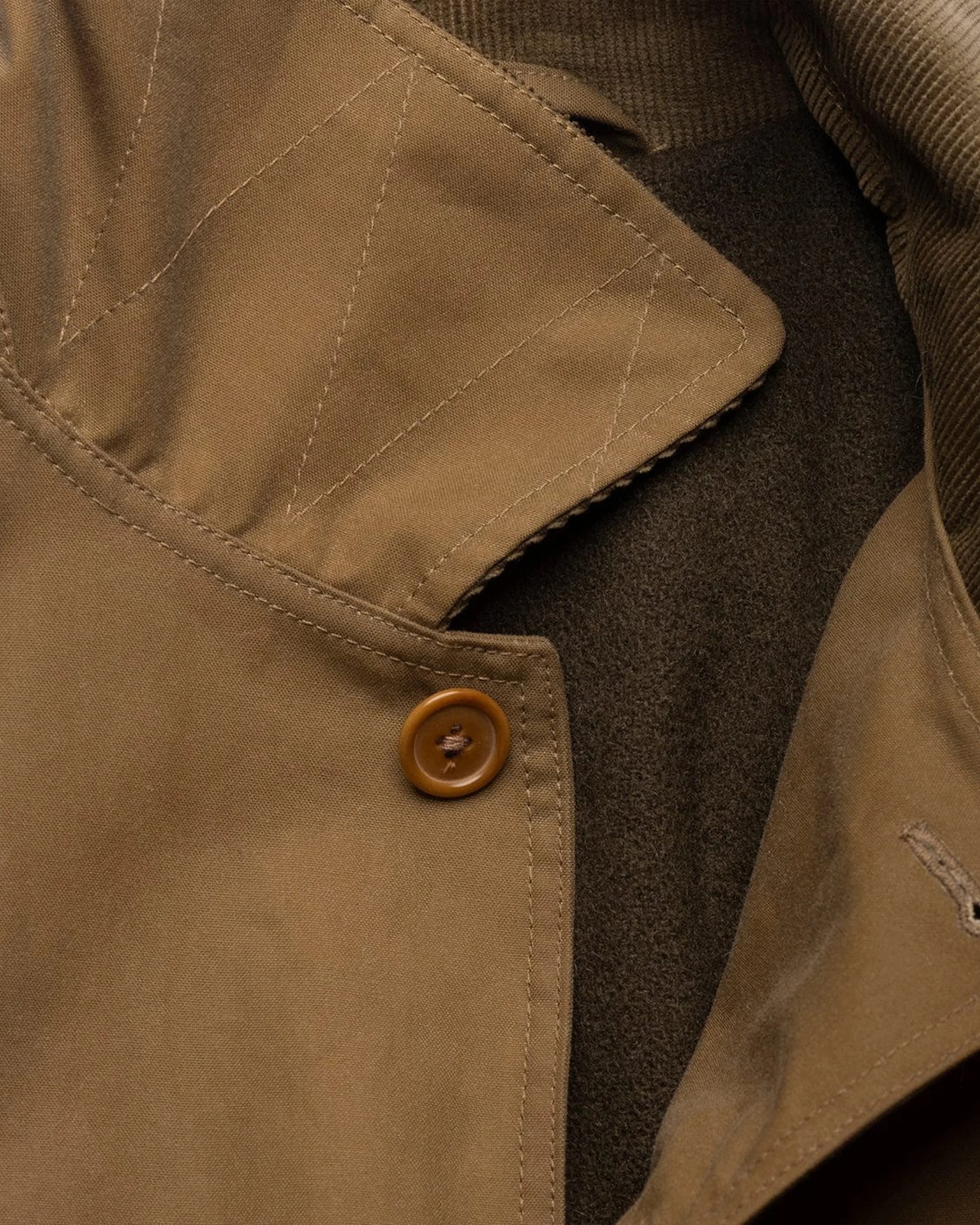 Close-up of a brown jacket collar with a button and visible stitching details.