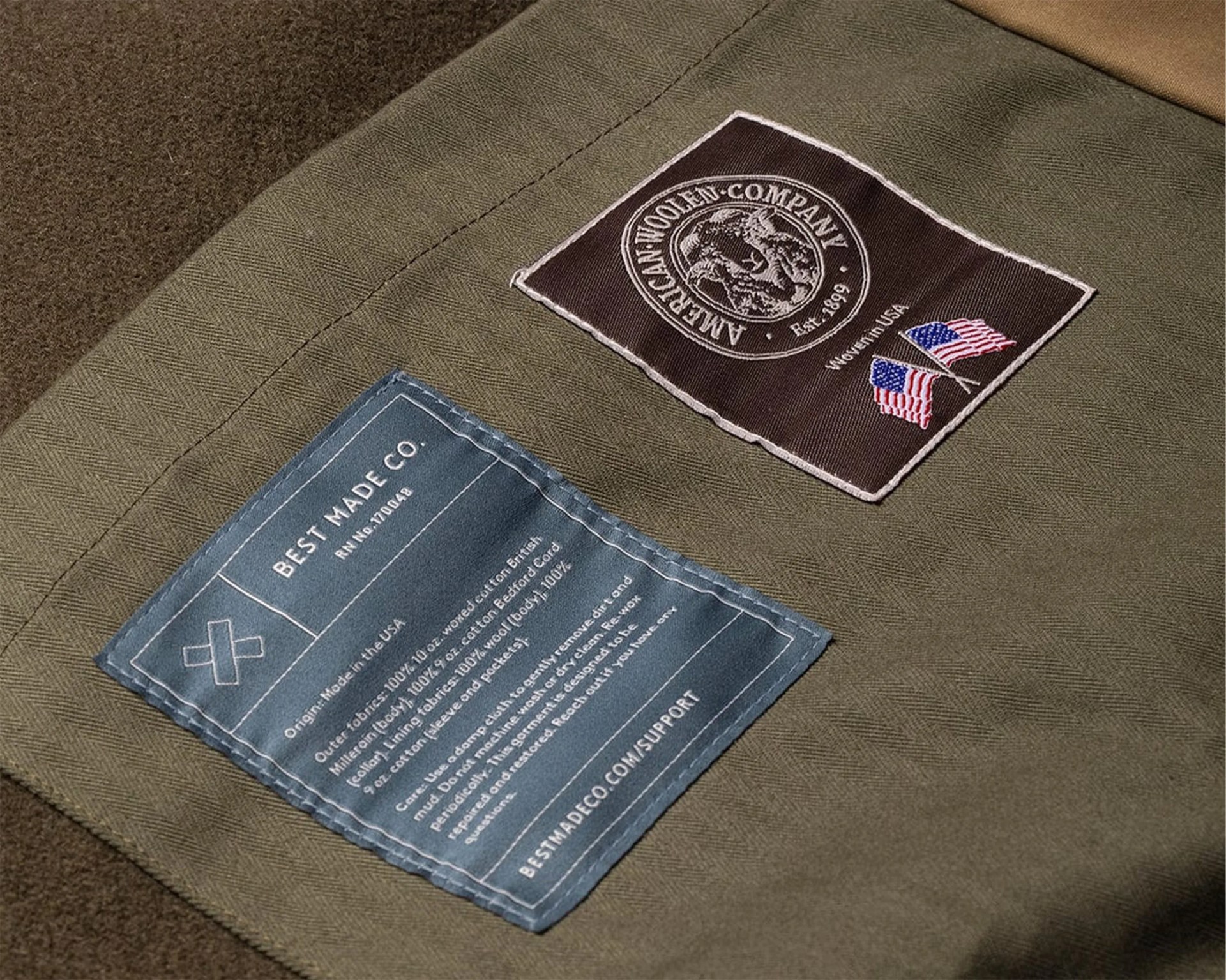 Two fabric labels on olive-green herringbone fabric, one brown with "American Woolen Company" and two American flags, the other blue with "Best Made Co." and care instructions.