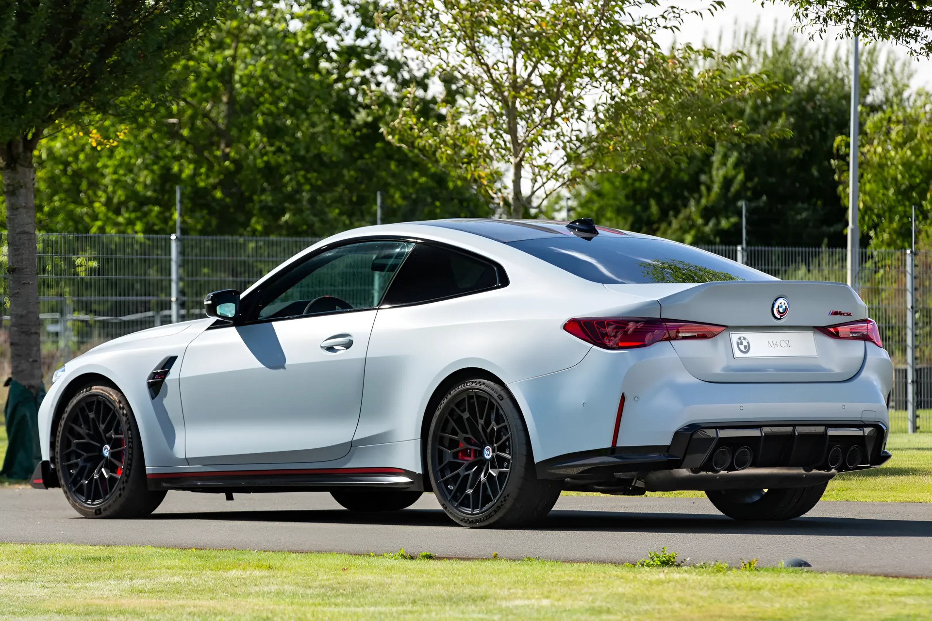 White BMW M4 CSL coupe with black wheels parked on a paved surface near grass and trees.