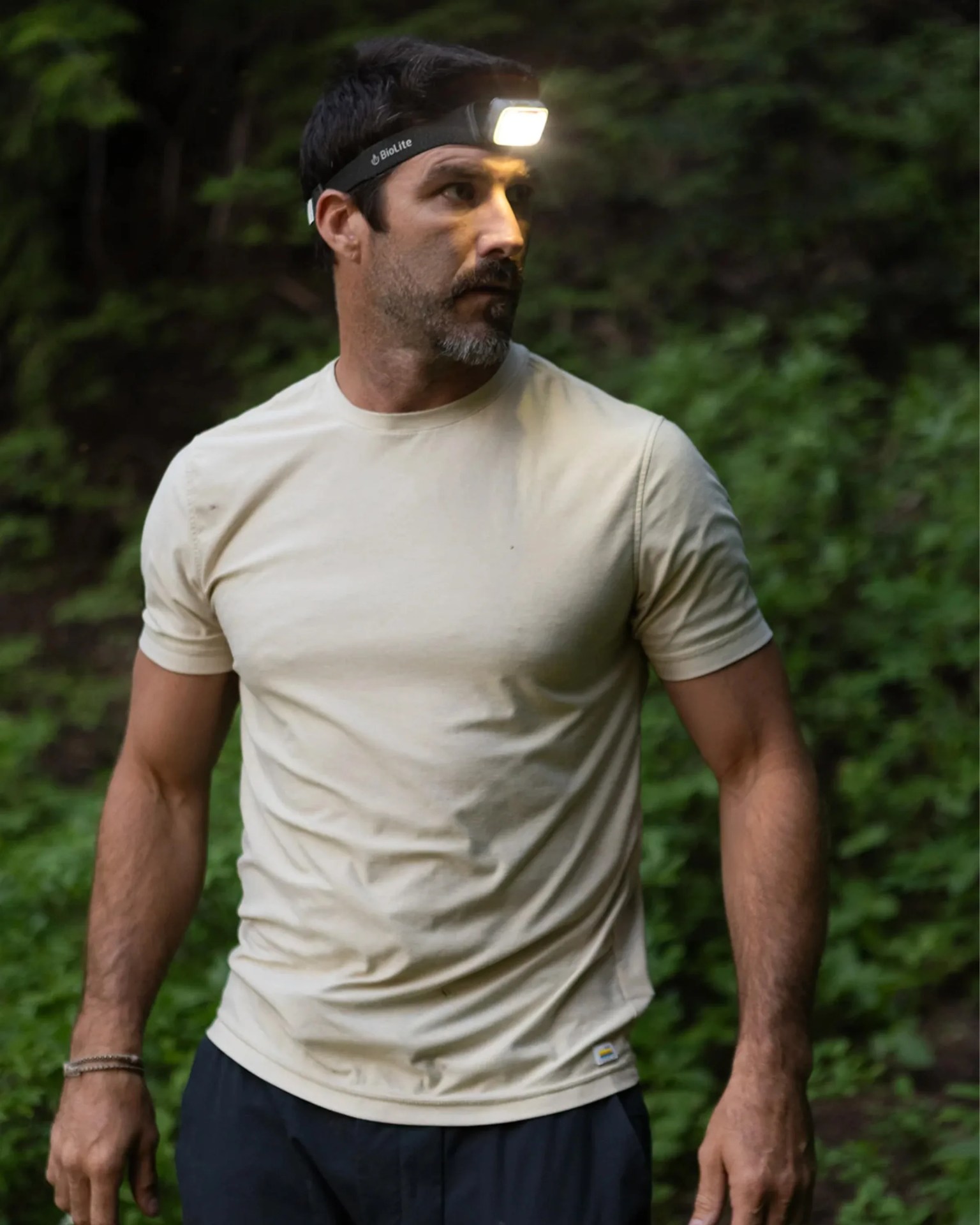 Man wearing a beige short-sleeve shirt and a black BioLite headlamp in a forest setting.