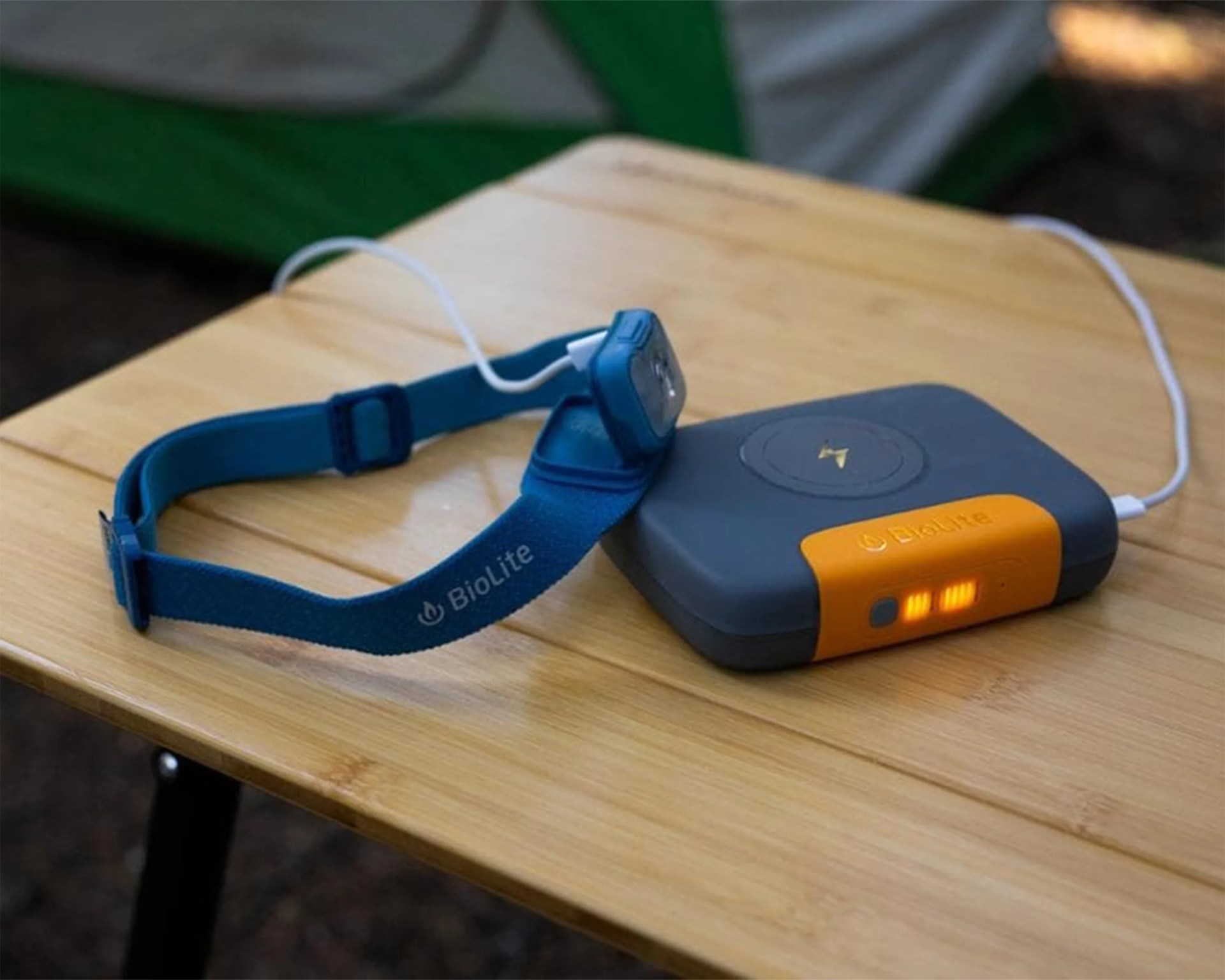 Blue BioLite headlamp with adjustable strap connected to a gray and orange charging device on a wooden table.