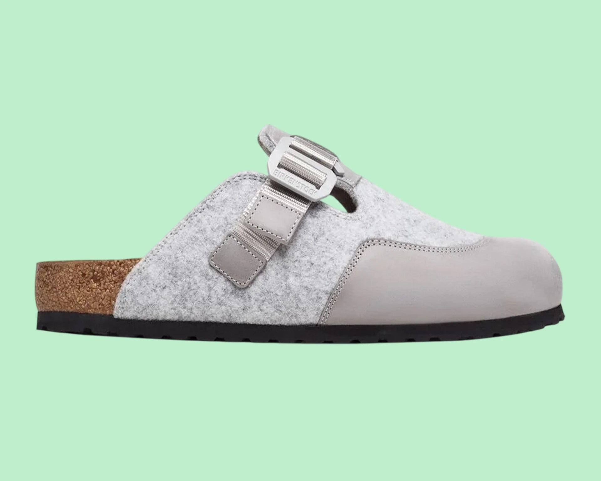 Light gray felt and leather slip-on clog with adjustable strap and cork footbed on a mint green background.