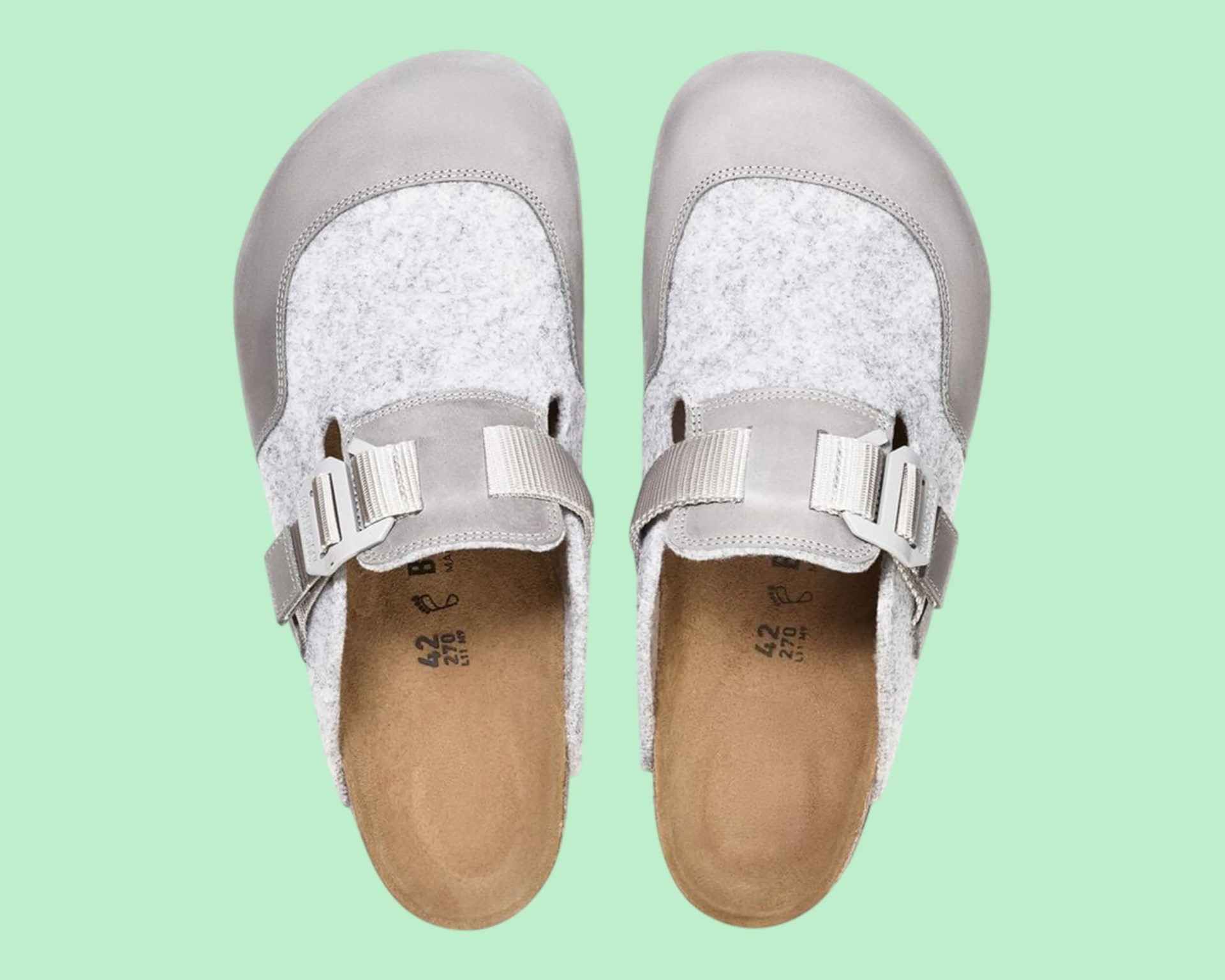 Pair of gray felt and leather slip-on clogs with adjustable straps and cork footbeds on a green background.