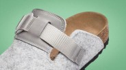 Gray felt slip-on clog with adjustable gray strap and brown footbed on green background.
