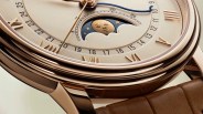 Close-up of a gold watch face with Roman numerals, a moon phase indicator, and a brown leather strap.