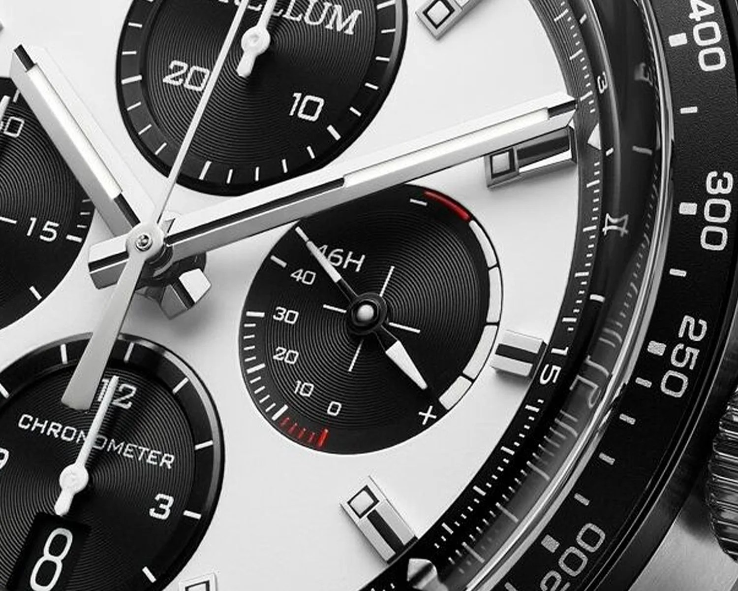 Close-up of a black and white chronograph watch face with silver hands and subdials, featuring tachymeter markings on the bezel.